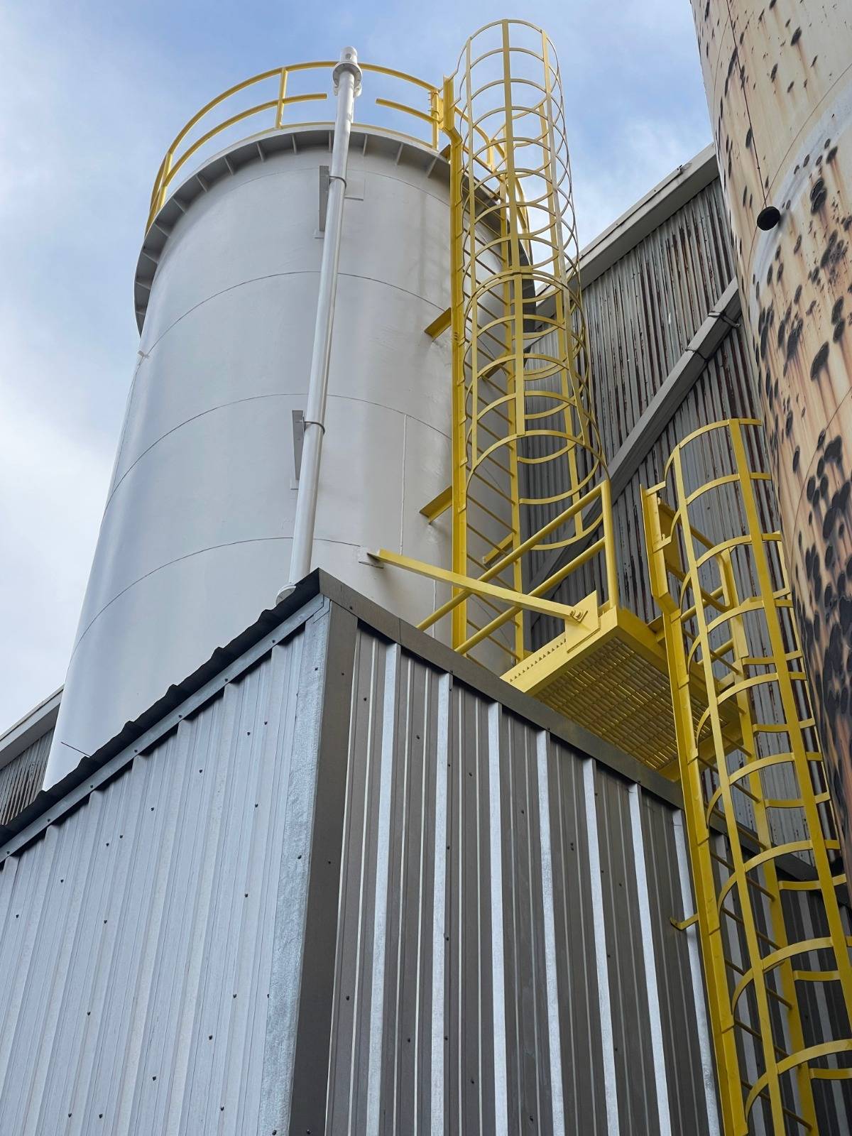 Yellow caged ladder and platform installed on an industrial tank
